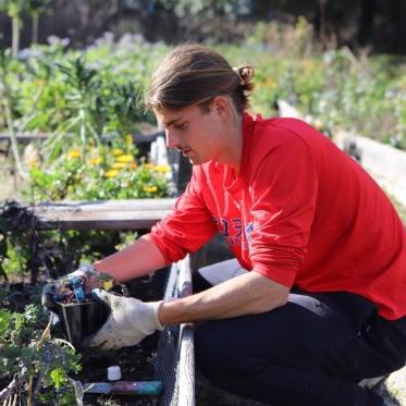 male presenting student gardening at the legacy garden